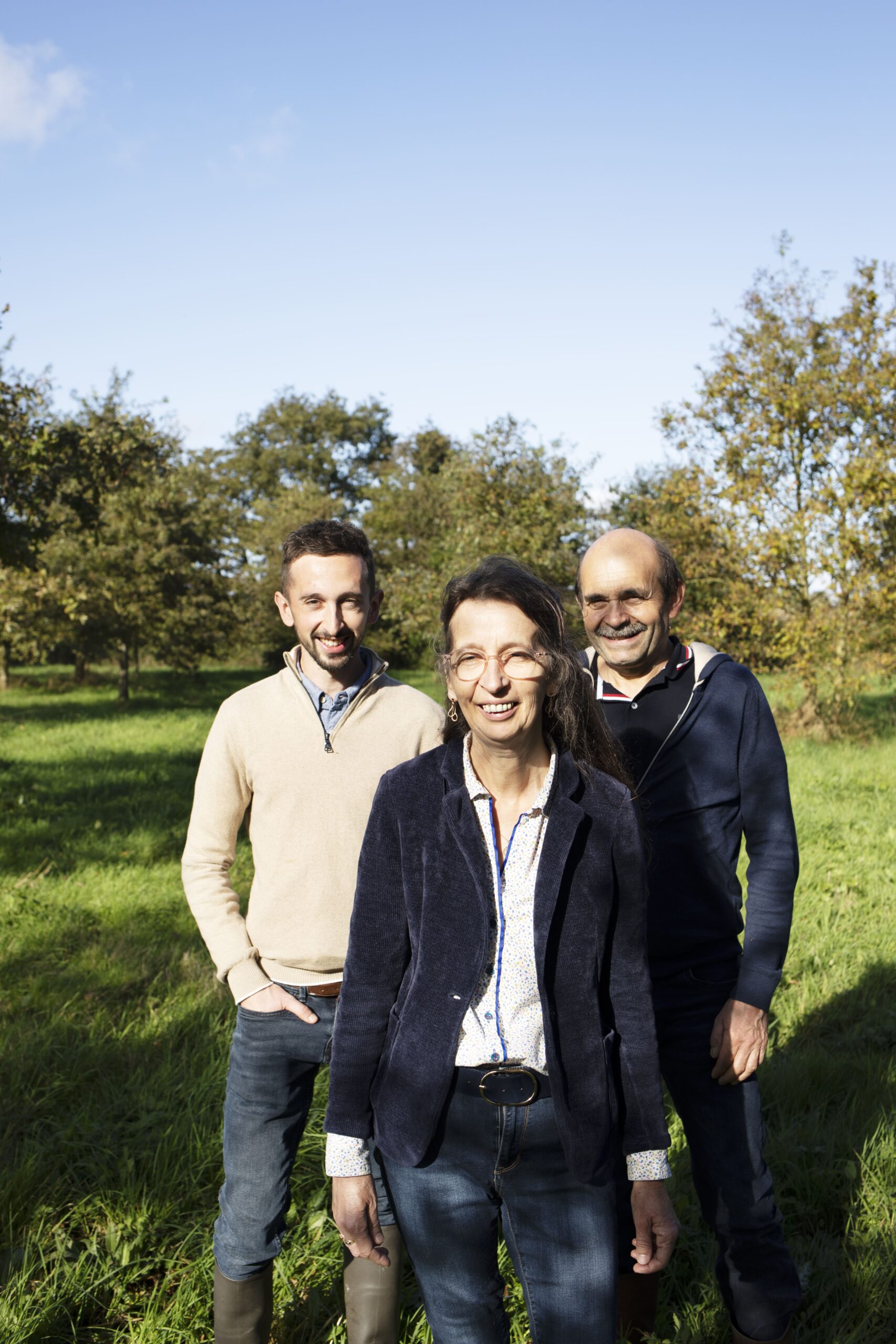 Portrait de trois éleveurs souriants dans un champ, représentant une équipe engagée dans l’agriculture durable et l’élevage biologique.